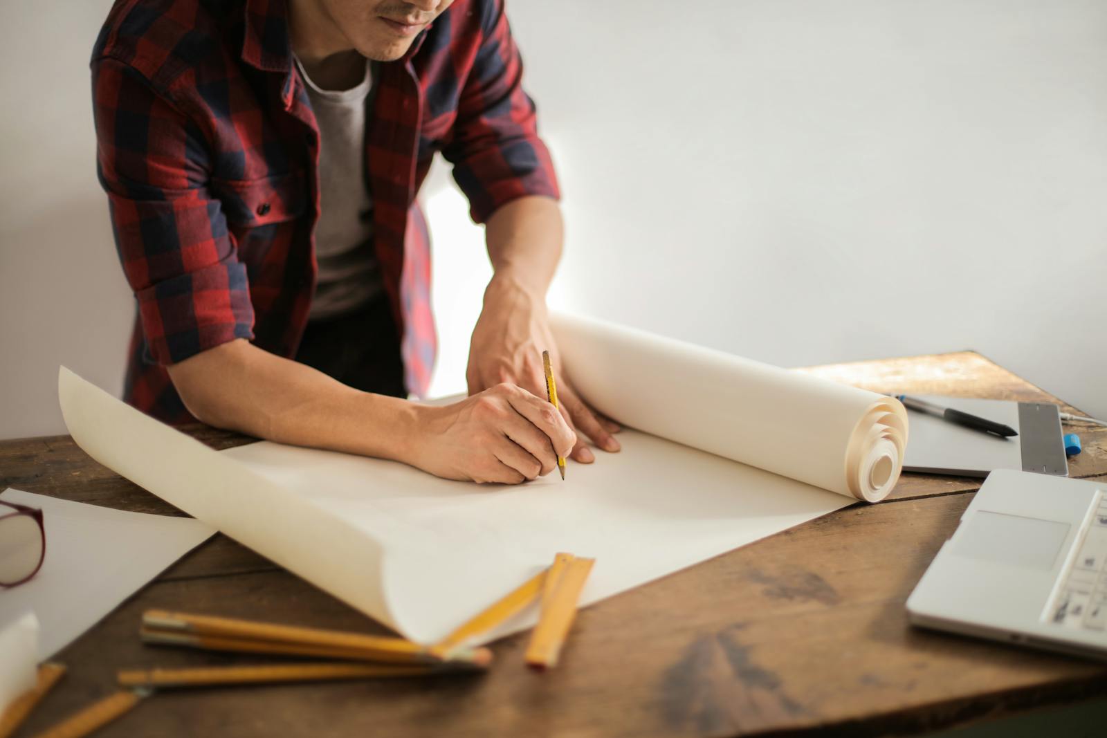 A focused architectural designer drafting blueprints at a desk indoors.